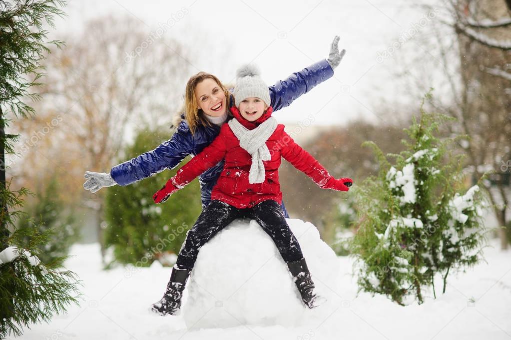Young woman and girl of school age build a snowman.