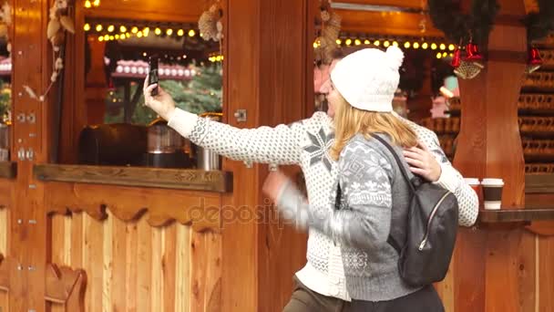 Bazar de Natal. O jovem casal é fotografado perto do pavilhão de madeira decorado festivamente . — Vídeo de Stock