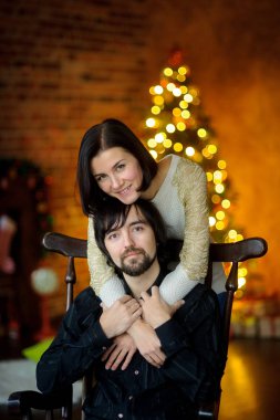 Noel akşamı. Genç kadın bir sandalyede oturan adam kucaklayan.