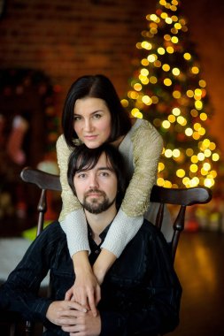 Noel akşamı. Genç kadın bir sandalyede oturan adam kucaklayan.