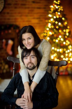 Noel akşamı. Genç kadın bir sandalyede oturan adam kucaklayan.