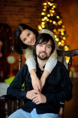 Noel akşamı. Genç kadın bir sandalyede oturan adam kucaklayan.