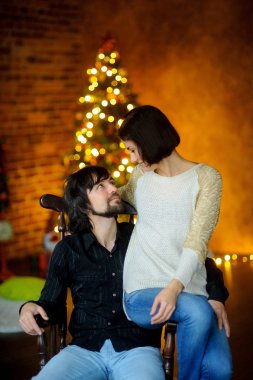 Noel akşamı. Genç kadın bir sandalyede oturan adam kucaklayan.