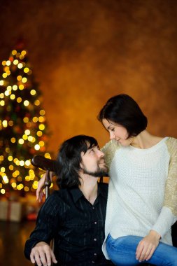 Noel akşamı. Genç kadın bir sandalyede oturan adam kucaklayan.