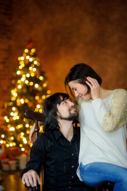 Noel akşamı. Genç kadın bir sandalyede oturan adam kucaklayan.