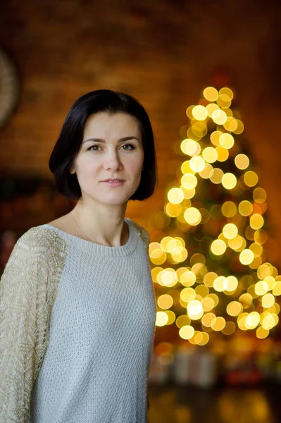 Elegantemente vestida jovem está contra o fundo da árvore de Natal — Fotografia de Stock