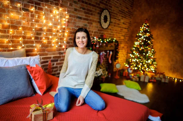 Navidad. Linda mujer joven se sienta en la cama grande y sonríe alegremente . — Foto de Stock