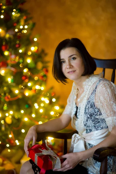 Mujer joven elegantemente vestida se sienta en mecedora cerca del árbol de Navidad . — Foto de Stock