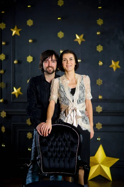 Young couple stands against the background of festively decorated dark wall. — Stock Photo, Image