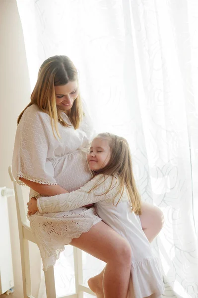 Charmant klein meisje haar zwangere moeder knuffelen. — Stockfoto