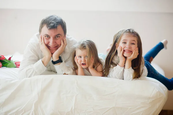 De jonge vader en twee van zijn charmante kleine dochters liggen op een bed. — Stockfoto
