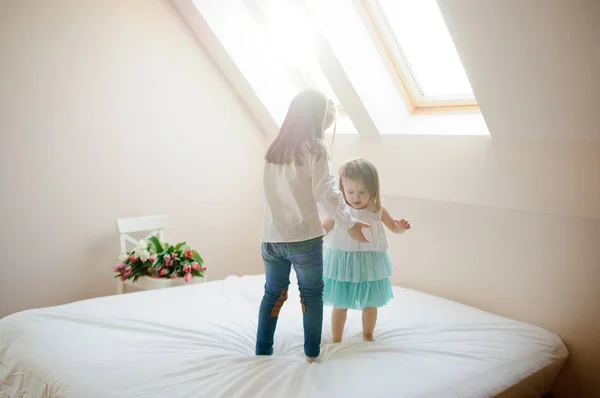 Two little sisters dance on a big bed. — Stock Photo, Image