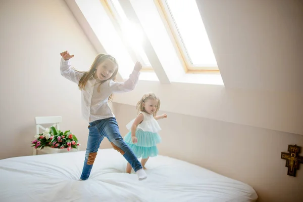 Two little sisters dance on a big bed. — Stock Photo, Image