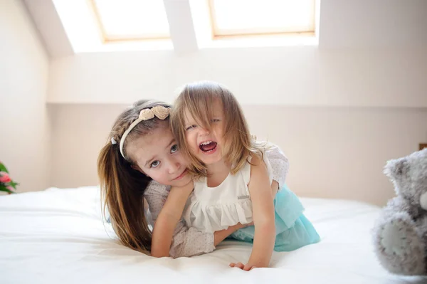 Auf einem großen Bett liegen zwei kleine Schwestern in einer Umarmung. — Stockfoto