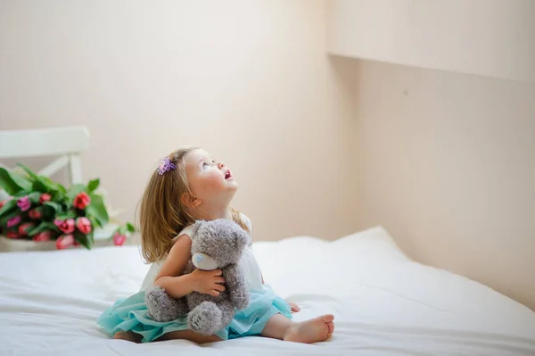 Het charmante kleine meisje zit blote voeten op een groot bed. — Stockfoto