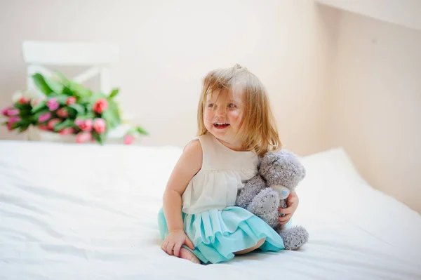 La encantadora niña se sienta en una cama grande . —  Fotos de Stock
