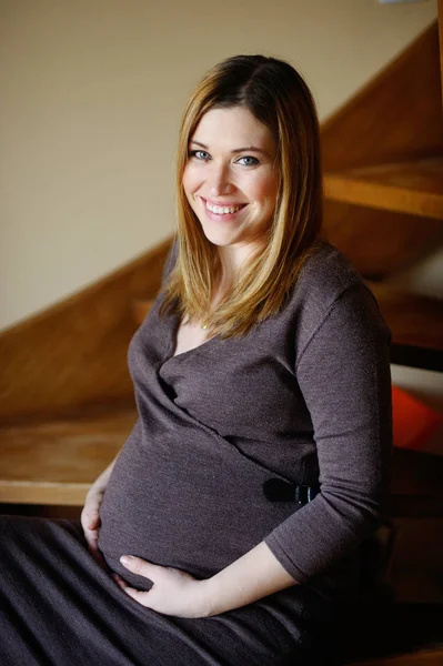 Güzel genç hamile kadın bir ahşap merdiven basamaklarında oturur.