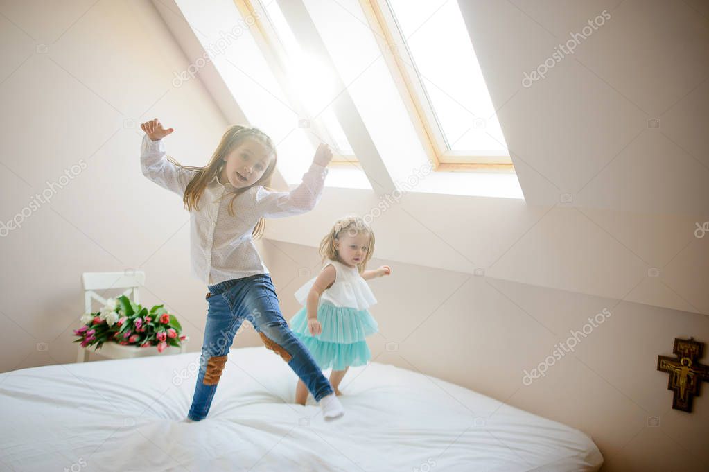 Two little sisters dance on a big bed.