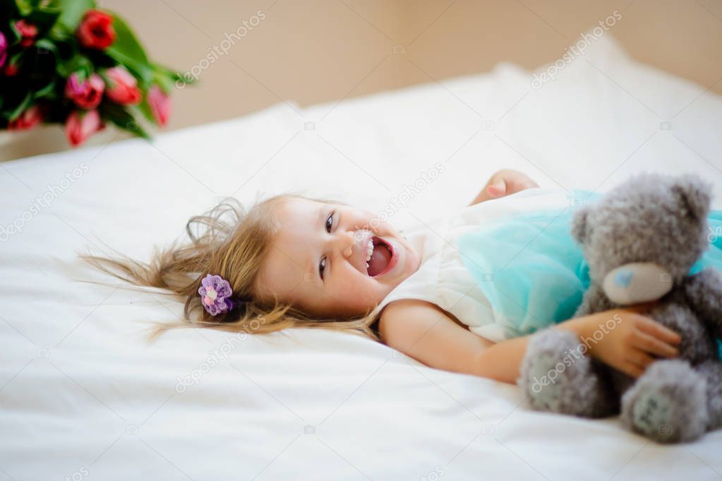 The charming little girl lies on a big bed.