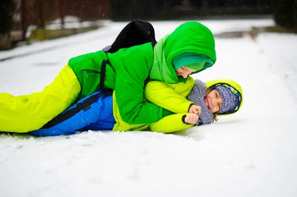 Dos chicos en overoles brillantes de invierno juegan en la nieve . — Foto de Stock