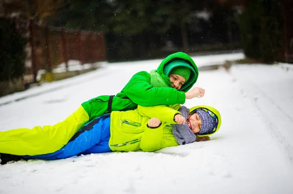 Dos chicos en overoles brillantes de invierno juegan en la nieve . — Foto de Stock