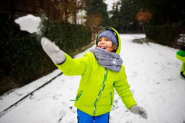 The cheerful boy of school age plays snowballs.