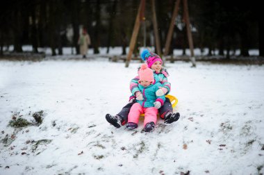 İki küçük kız birlikte bir tepeden uçan daire kızağa aşağı taşı.