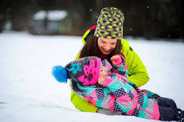 Adorável jovem mulher e menina em jaquetas brilhantes mentira na neve . — Fotografia de Stock