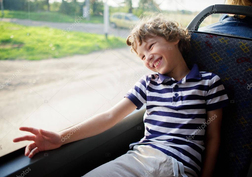 The cheerful little boy in a striped t-shirt goes by the bus.