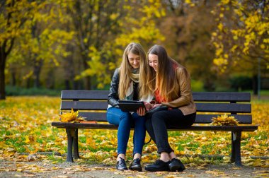 Erken sıcak sonbahar. İki sevimli kız sonbahar parkta bir bankta oturup.