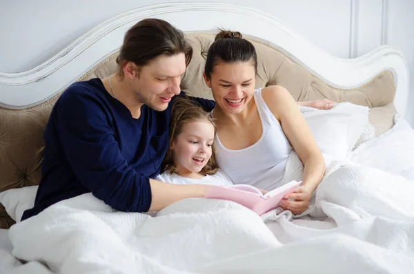 The little daughter reads to parents the book.