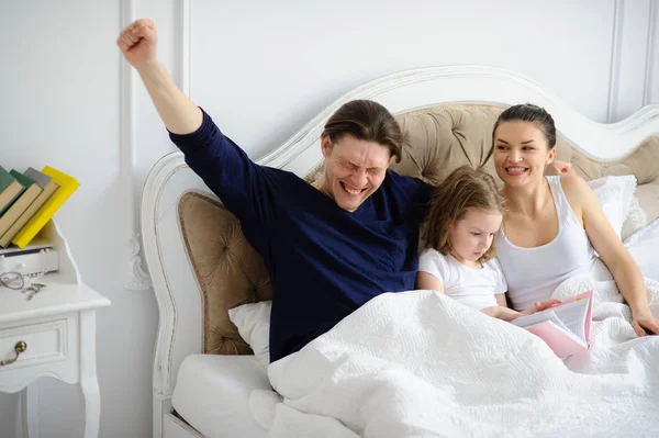 The little daughter reads to parents the book.