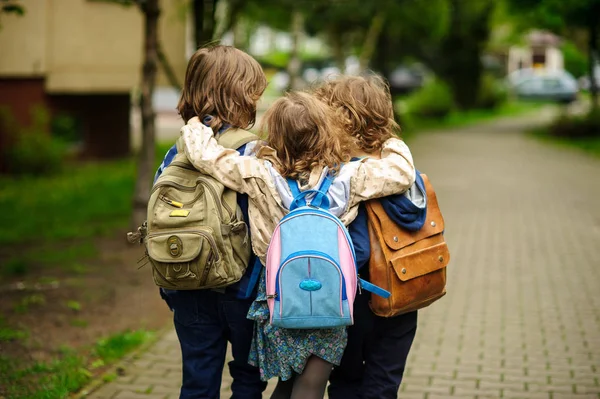 Tre små elever gå i en omfamning i skolan. — Stockfoto