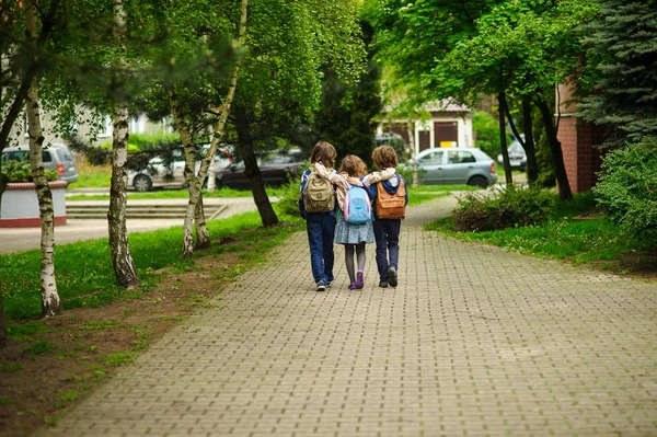 Three little school students, two boys and the girl, go in an embrace to school — Stock Photo, Image