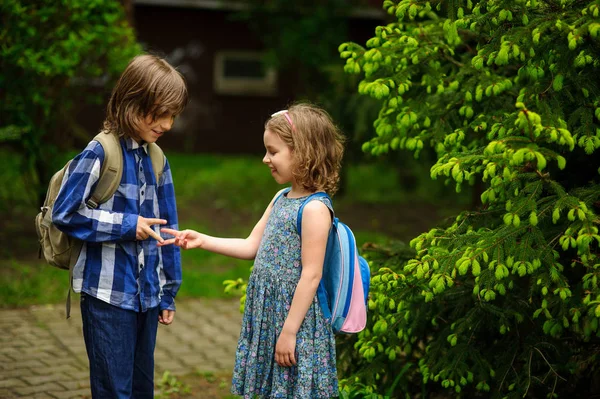 Deux petits écoliers, le garçon et la fille, communiquent joyeusement sur la cour de l'école . — Photo