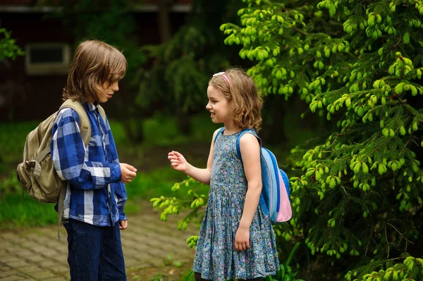Två små skolelever, pojken och flickan, kommunicera glatt på skolgården. — Stockfoto