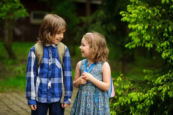 Dos pequeños estudiantes se comunican alegremente en el patio de la escuela . — Foto de Stock