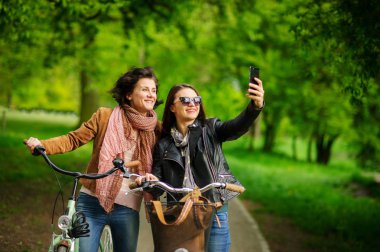İki güzel genç kadın Parkta yürümek selfies Bisiklet sırasında yapmak.