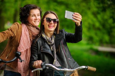 İki güzel genç kadın Parkta yürümek selfies Bisiklet sırasında yapmak.