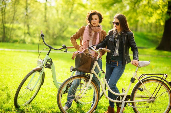 Two young attractive women ride bikes in the spring park. — Stock Photo, Image