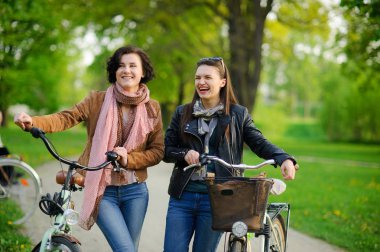 Bisiklet üzerinde iki çekici genç kadın bahar Parkta yürümek.