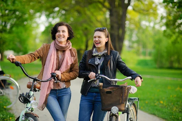 Two charming young women on bicycle walk in the spring park.