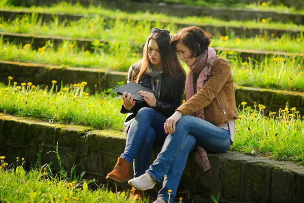 İki genç çekici kadın tablet ellerde ile taş adımları oturmak. — Stok fotoğraf