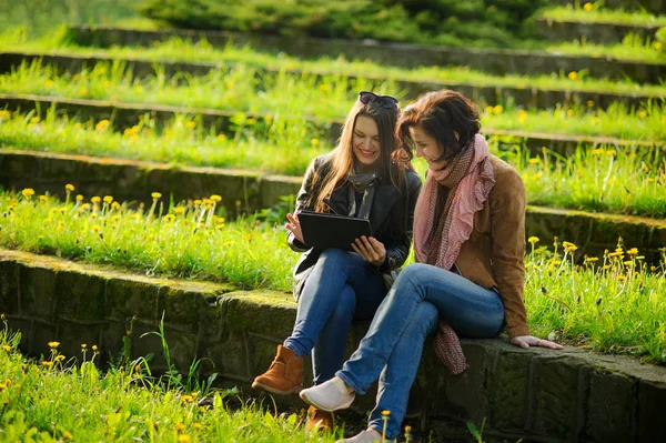 Twee jonge charmante vrouwen zitten op stenen trappen met de tablet in handen. — Stockfoto