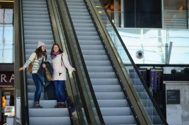 Havaalanındaki yürüyen merdiven üzerinde küçük Bagaj ile iki genç kadın.