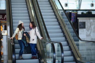 Havaalanındaki yürüyen merdiven üzerinde küçük Bagaj ile iki genç kadın.