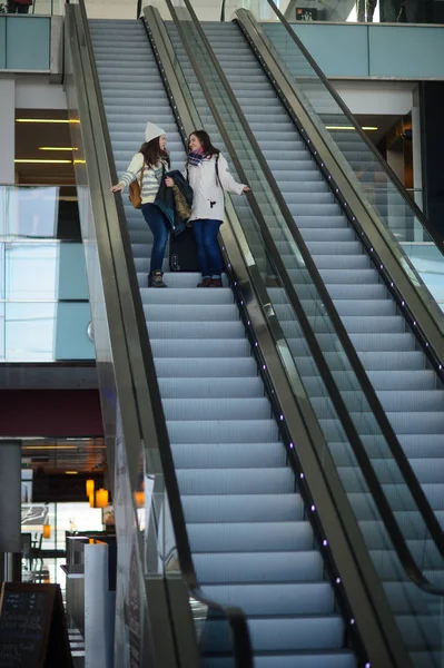 Δύο νεαρές γυναίκες με μικρές αποσκευές για τις κυλιόμενες σκάλες στο αεροδρόμιο. — Φωτογραφία Αρχείου