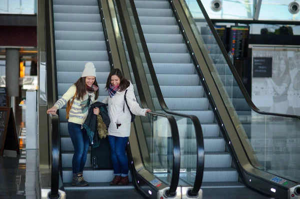 Δύο νεαρές γυναίκες με μικρές αποσκευές για τις κυλιόμενες σκάλες στο αεροδρόμιο. — Φωτογραφία Αρχείου