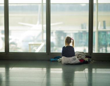 Hava alanında büyük bir pencere yakınında küçük kız oturur.