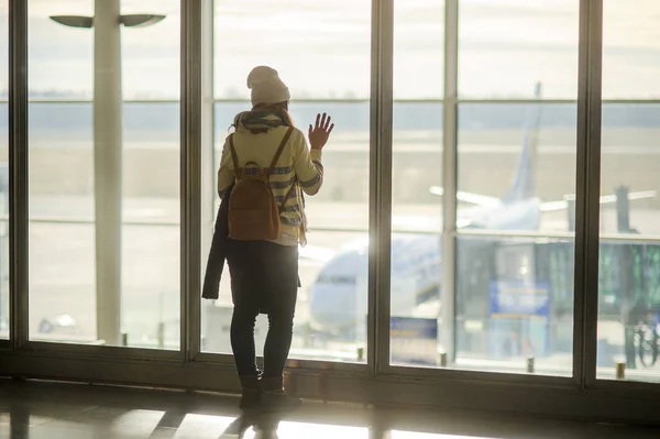 Eine Frau mit Rucksack steht am großen Fenster des Flughafens. — Stockfoto